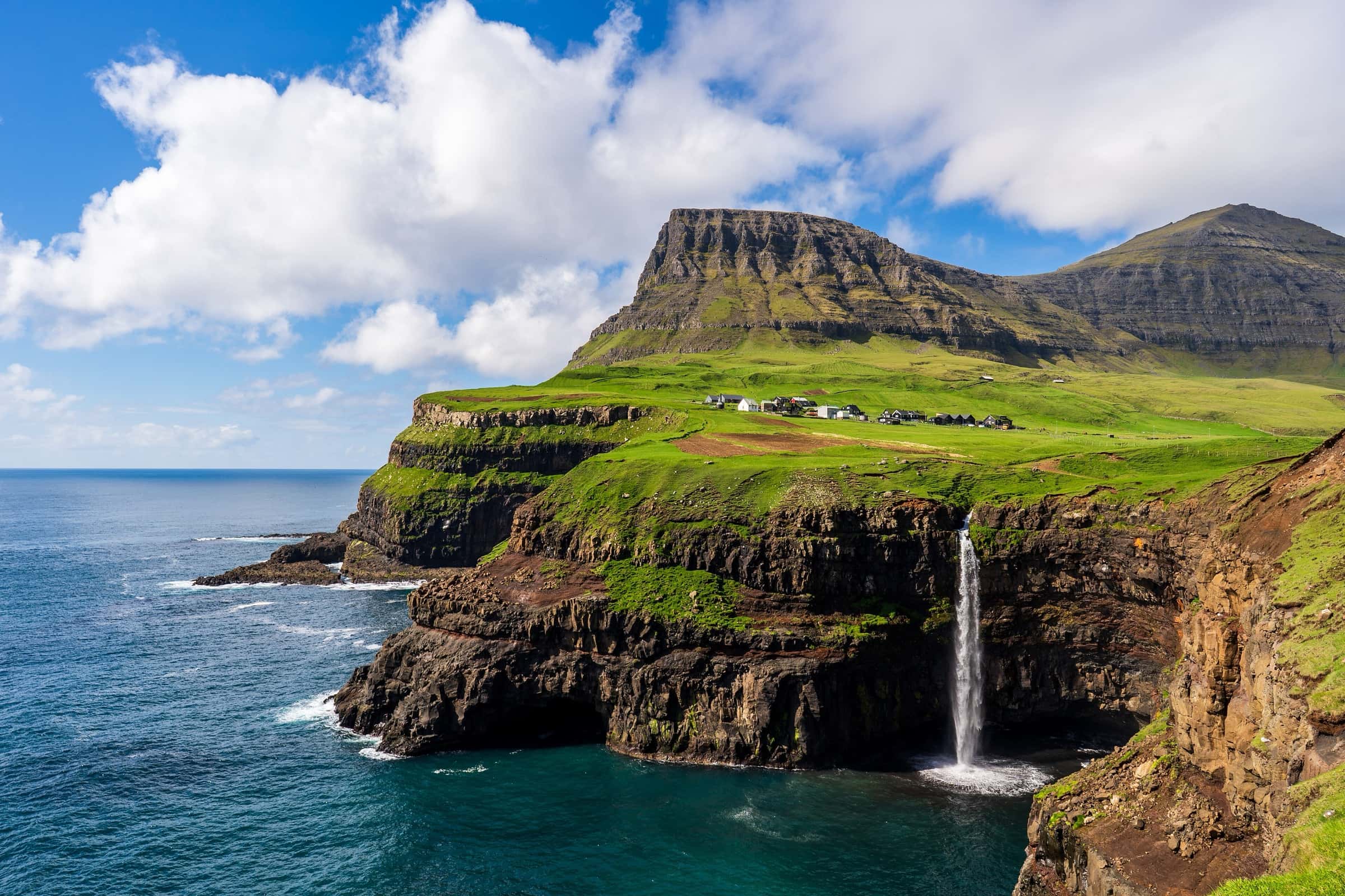 Gásadalur village above sea cliffs, with Múlafossur waterfall dropping into the Atlantic