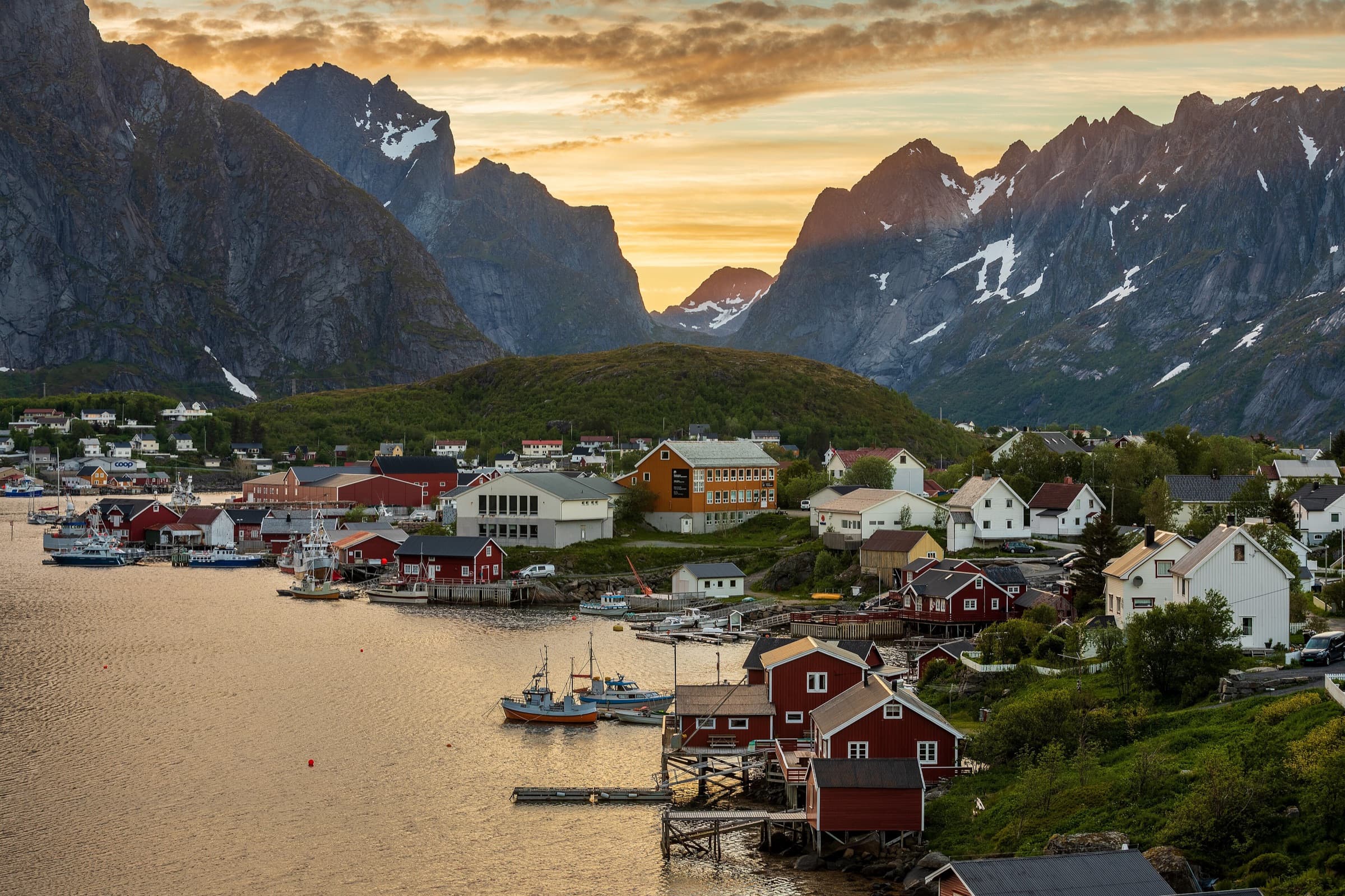Red and white houses of Reine beneath jagged Lofoten peaks in warm evening light