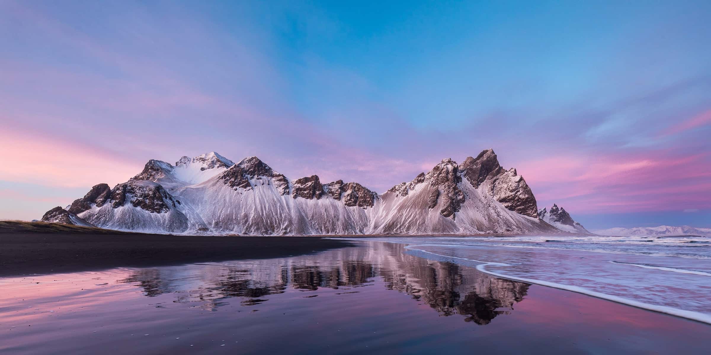 Vestrahorn mountain at sunset under a pink sky, mirrored in the tidal lagoon at Stokksnes