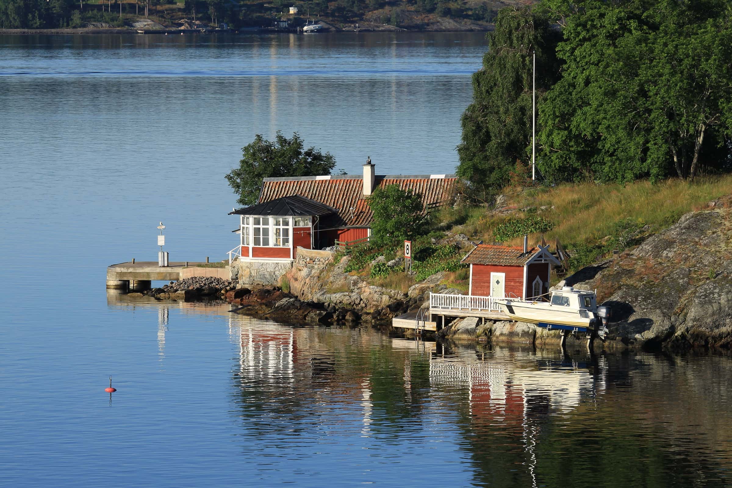 A red wooden cottage with a small jetty on a rocky islet in the Stockholm archipelago