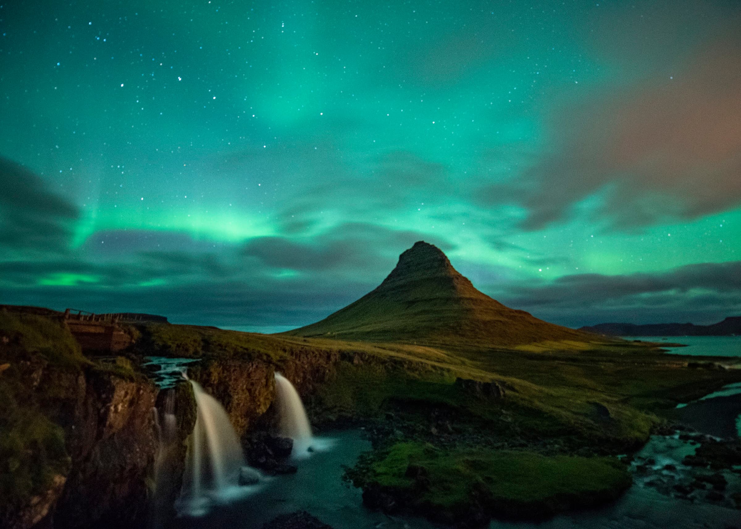 Green aurora borealis arcing over Kirkjufell mountain and its waterfalls at night